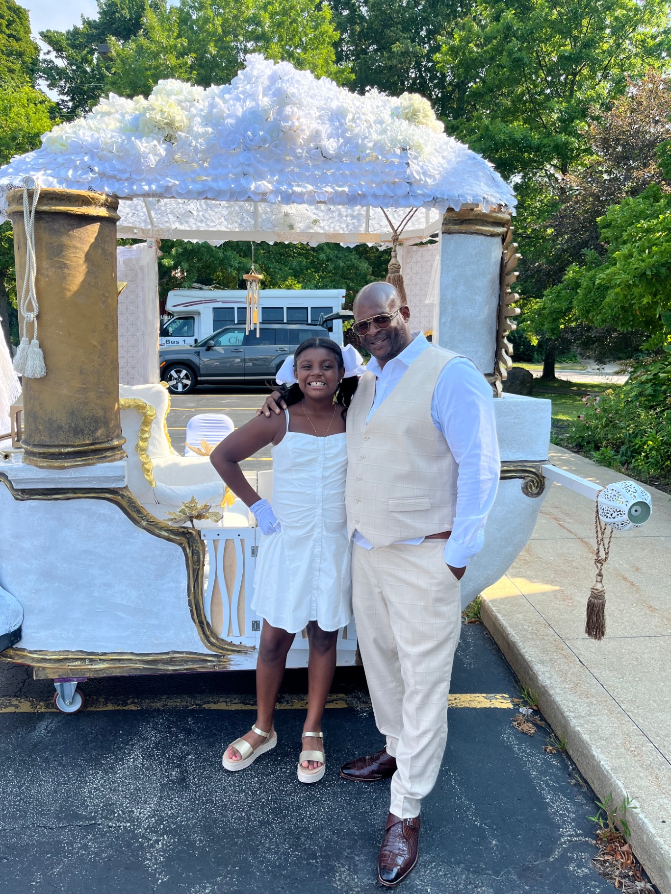 Push Me Dad founder and his daughter, dressed in white and gold, smiling together in front of an ornate white carriage
